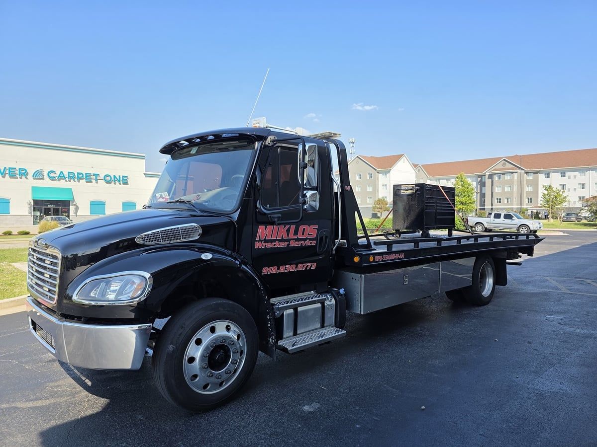Miklos-branded flatbed tow truck with black containers on its bed
